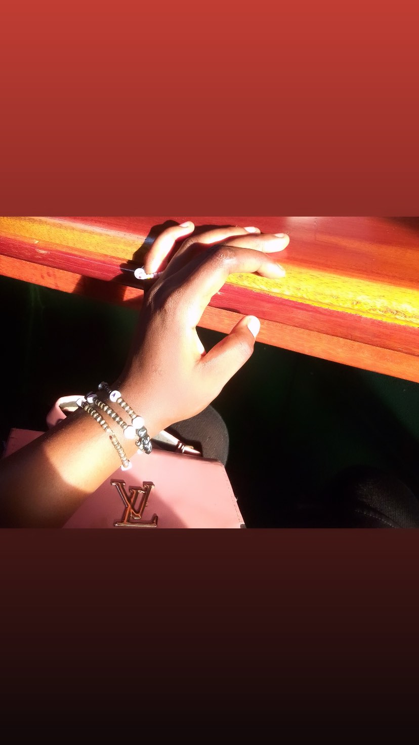 Hand with white nails and jewelry holding a pink Louis Vuitton bag against a dark background